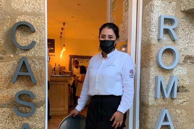 Raquel poses in uniform with a tray at the entrance to Casa Román.
