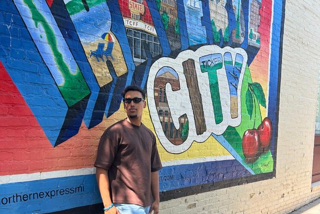 Michael Peguero poses in sunglasses in front of the Traverse City mural in Michigan.